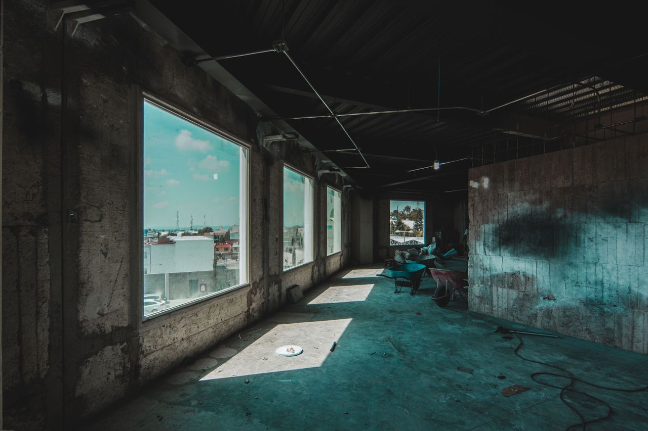 An urban industrial space under renovation with sunlight casting shadows through large windows.