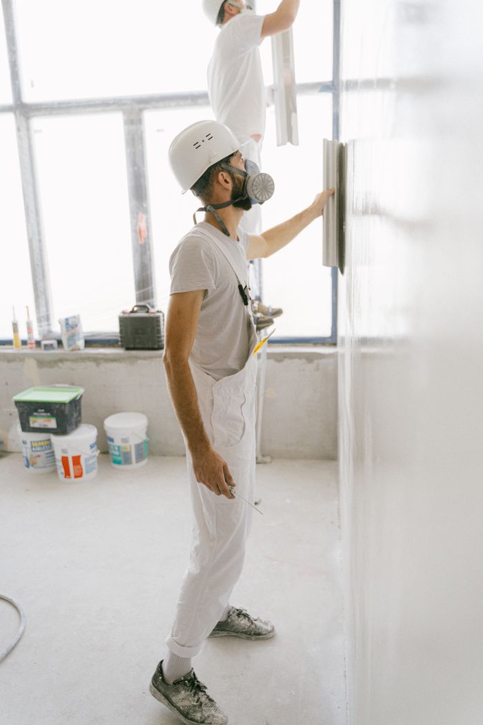 about-img Construction workers wear protective gear while plastering a wall indoors during home renovation.