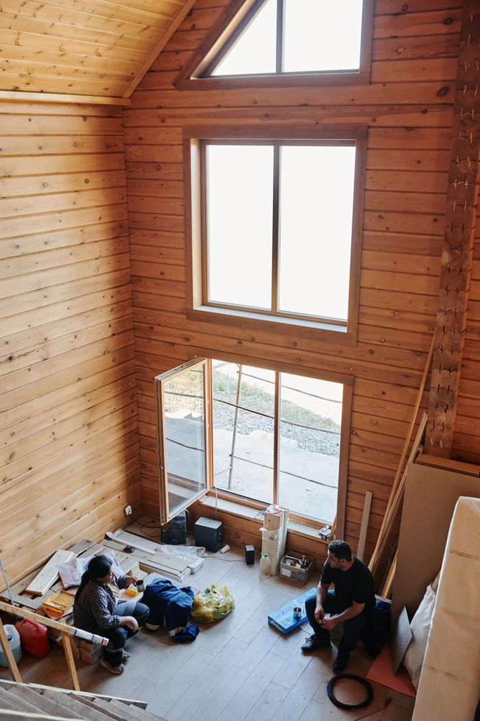our-mission Interior of a rustic wooden cabin with two people resting amid construction materials, capturing a moment of pause.